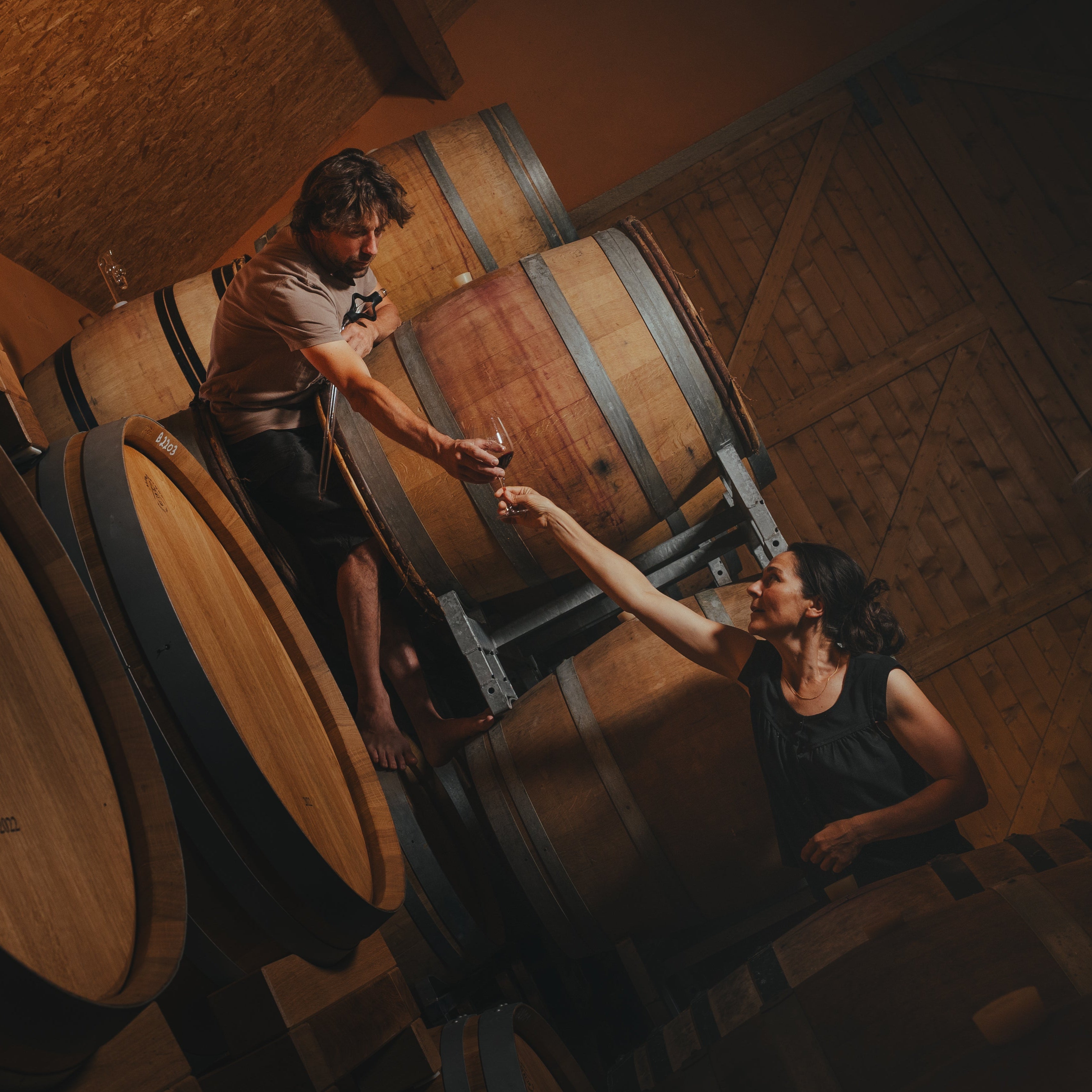 Paola and Flow people shaking hands in a wine cellar with wooden barrels at Domaine FloBusch