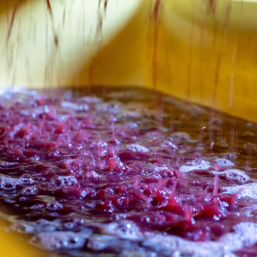Close-up of red wine liquid being poured into a container with bubbles.