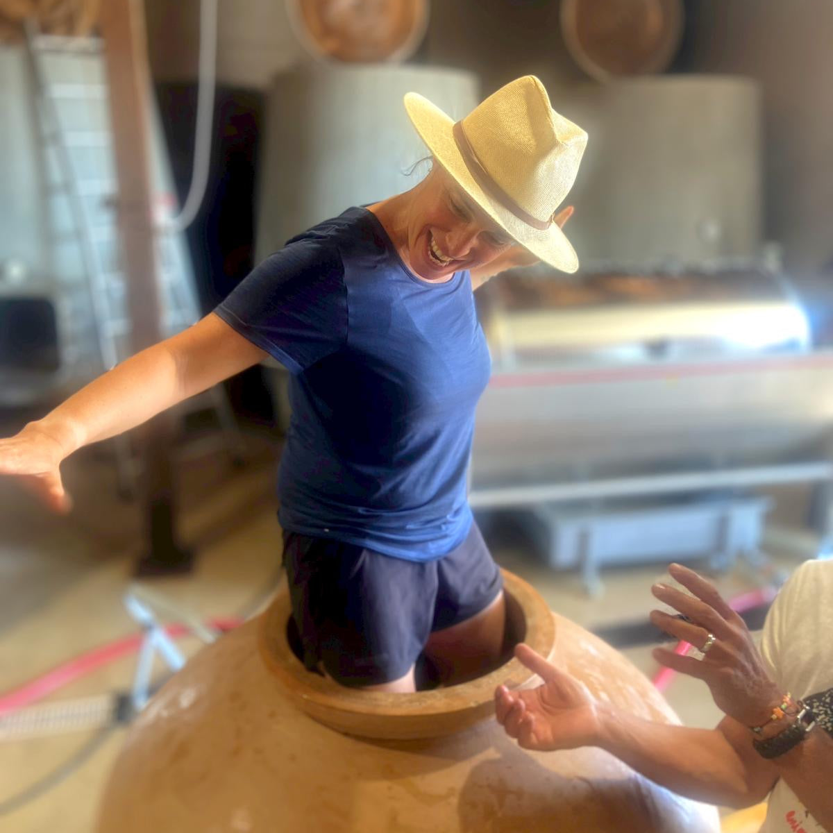 A person wearing a straw hat inside a large wine amphora 