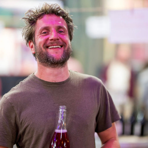 Mas Zenitude Julien Beluche holding a bottle of natural wine with a blurred background