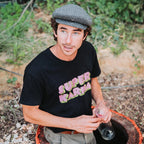 Raf Raybois, wearing a black t-shirt with 'Super Karma' text, sitting on a qvevri  outdoors.